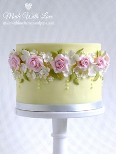 a yellow cake with pink roses and white flowers on the top is sitting on a stand