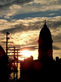 the sun is setting behind some buildings and power lines in the foreground, with clouds in the background