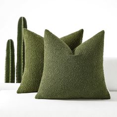 three green pillows sitting on top of a white couch next to cacti plants