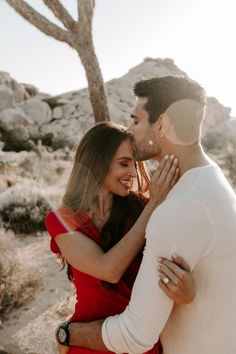 a man and woman embracing each other in front of a desert tree with rocks on the ground