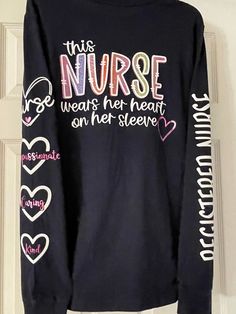 "This navy blue long sleeve crew neck tee is a 100% cotton design for breath-ability and comfort. This comfortable foundation features a solid tone that can be styled easily with your look. Item is also machine washable.  \"This NURSE wears her heart on her sleeve\" design on the back with Registered Nurse down right sleeve and 4 hearts cascading down the left sleeve. The four hearts down the left sleeve say Nurse, Compassionate, Caring, and Kind. The front left chest of the jacket has the nurse Navy Long Sleeve Top With Letter Print, Black Long Sleeve T-shirt With Heart Graphic, Navy Long Sleeve Relaxed Fit T-shirt, Navy Relaxed Fit Long Sleeve T-shirt, Long Sleeve Heart Graphic T-shirt For Fall, Long Sleeve T-shirt With Heart Graphic For Fall, Fall Long Sleeve Heart Graphic T-shirt, Fall Long Sleeve T-shirt With Heart Graphic, Navy Blue Long Sleeve