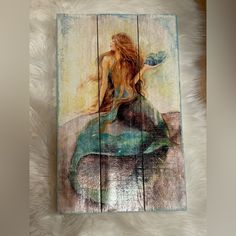 a painting of a mermaid sitting on top of a wooden plank