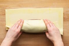 two hands rolling out dough on top of a wooden table with a piece of bread in the middle