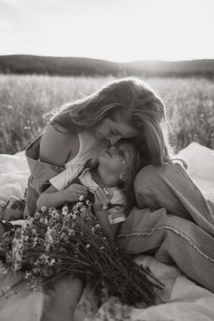 two women are laying on a blanket with flowers in their hands and one woman is hugging the other