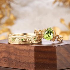 two gold rings with green stones on top of a wooden table next to each other