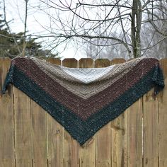 a knitted shawl hanging on a wooden fence in front of a tree with no leaves