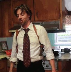 a man with suspenders and a tie standing in a kitchen next to an oven