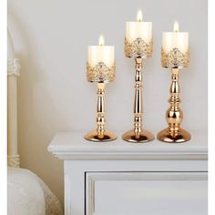 three gold candles sitting on top of a white dresser