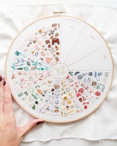 a woman's hand is holding up a cross stitch pattern on a white surface