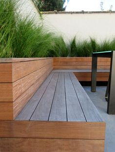 a wooden bench sitting on top of a cement floor next to tall grass and plants