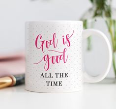 a coffee mug with the words god is good all the time next to a pen