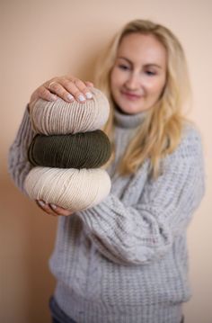 a woman holding three balls of yarn in her hands