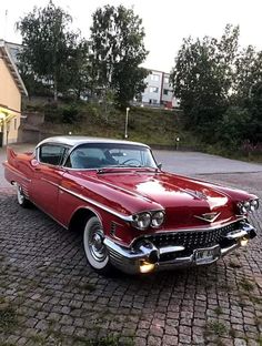 an old red car is parked in front of a house on a cobblestone driveway