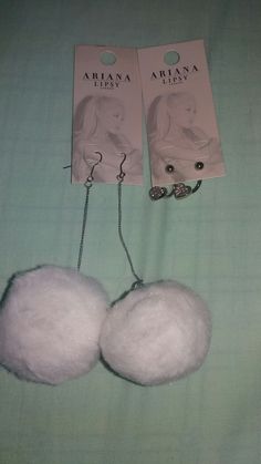 two white fluffy balls on a bed with tags attached to the back of each one