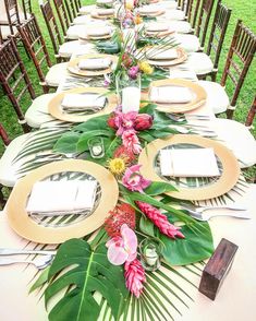 a long table set with place settings and flowers on the centerpieces is surrounded by greenery