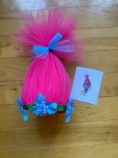 a pink wig with blue bows and a card on a wooden floor next to it