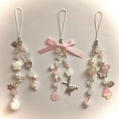 several charms are hanging from the side of a white surface with a pink ribbon on it