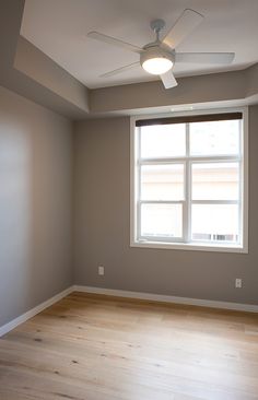 an empty room with hard wood floors and a ceiling fan in the corner between two windows