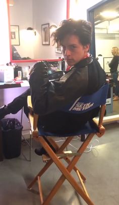 a young man sitting in a chair getting his hair cut by another person who is standing next to him