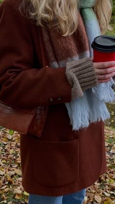 a woman holding a cup of coffee in her right hand and wearing a scarf around her neck