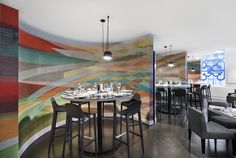 a dining room with tables and chairs in front of a colorful mural on the wall