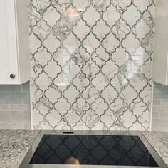 a kitchen with marble backsplash and white cabinetry in the backround