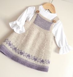 a knitted dress with buttons on the front and back, sitting next to a wooden hanger