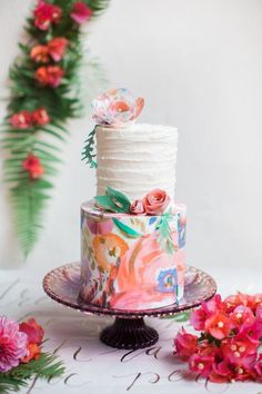 a multi layer cake with flowers on top sitting on a plate next to a flower arrangement