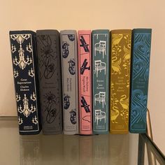 five books are lined up on a glass table in front of a white wall and stair case