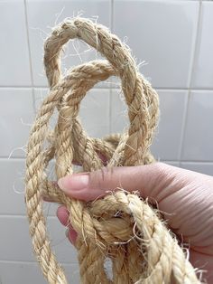 a hand holding rope in front of a white tile wall and tiled flooring behind it