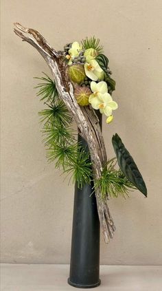 a vase filled with flowers and greenery on top of a white tablecloth next to a wall