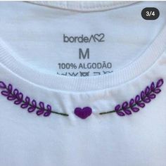 a white shirt with purple flowers and hearts on the front, embroidered onto it's chest