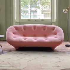 a pink couch sitting on top of a rug in a living room next to a window