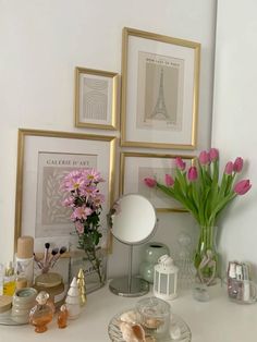 a white desk topped with pictures and vases filled with pink flowers on top of it