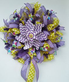 a purple, yellow and white wreath with polka dots on the bottom is decorated with ribbons