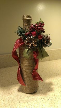 a wine bottle wrapped in twine and tied with red ribbon, decorated with pine cones, berries and holly