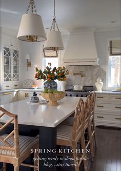 a kitchen with white cabinets and two hanging lights above the counter top is decorated with orange flowers