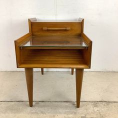 a small wooden table with glass top on concrete floor next to white wall and cement floor