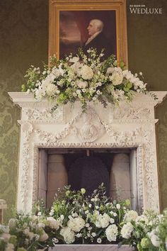 a mantel decorated with white flowers and greenery