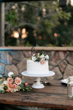 a white cake sitting on top of a wooden table next to some candles and flowers