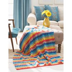 a crocheted blanket on a couch with yellow flowers in a vase next to it