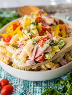 pasta salad with ham and vegetables in a white bowl on a blue towel next to cherry tomatoes