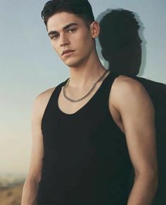 a young man wearing a black tank top standing in front of a wall with his shadow on it