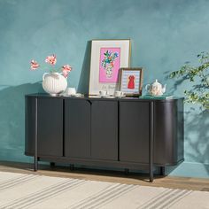 a sideboard with pictures and vases on it in front of a blue wall