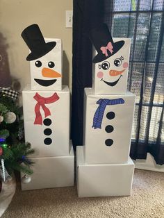 three snowmen made out of cardboard boxes sitting on the floor next to a christmas tree