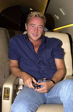 a man sitting in an airplane seat holding a cell phone and looking at the camera