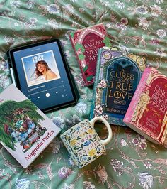 there are many books on the bed with mugs and an electronic device next to them