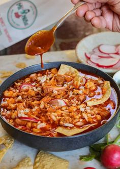 a person dipping some food into a bowl with tortilla chips on the side