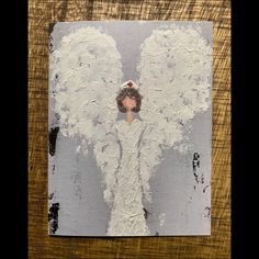 an angel painted on a piece of wood with white paint and black trim around the wings