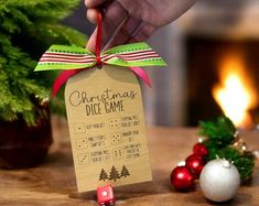 a hand holding a christmas dice game on top of a wooden table next to ornaments